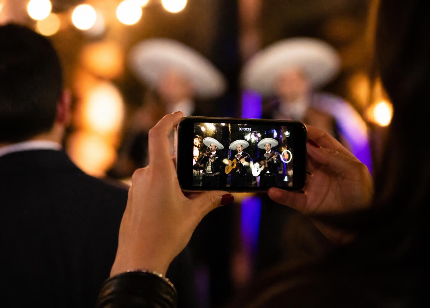 Persona grabando con su teléfono una presentación de mariachi en una fiesta.